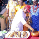 Prince Alex Mbata trying to have a taste of the new yam while Eze David Onuegwunwoke watches with other traditional rulers at the occasion.