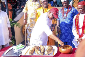 Prince Alex Mbata trying to have a taste of the new yam while Eze David Onuegwunwoke watches with other traditional rulers at the occasion.