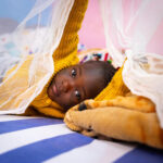 child-lying-on-bed-with-mosquito-net-in-cameroon