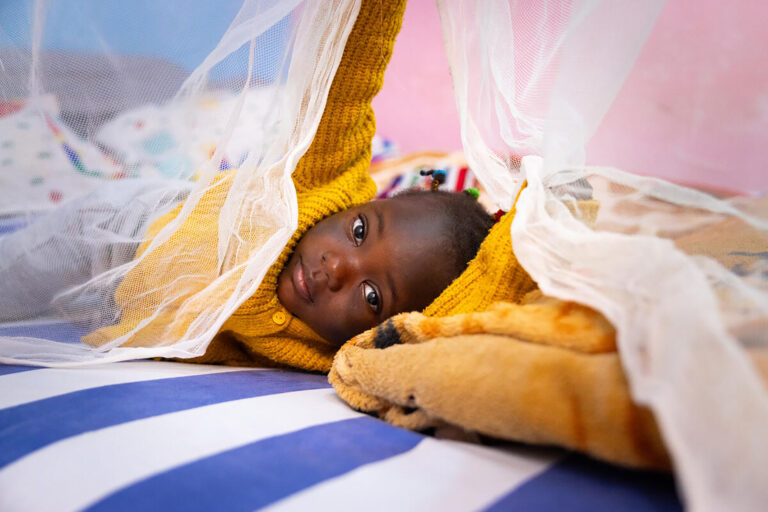 child-lying-on-bed-with-mosquito-net-in-cameroon